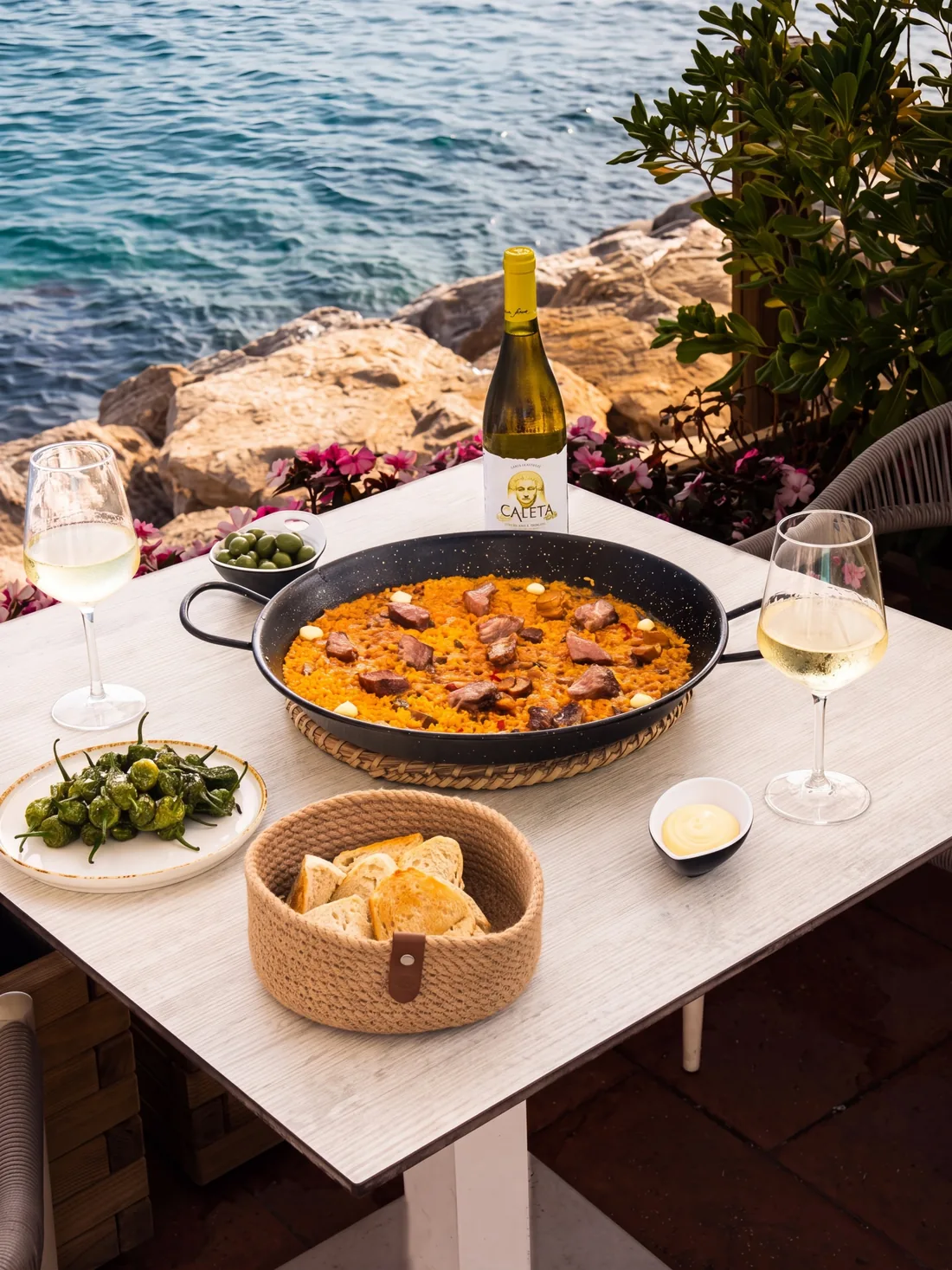 A paella and a bottle of white wine on a terrace table above the sea