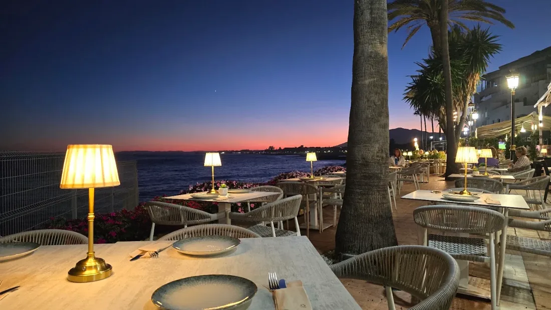 The Navaya terrace at dusk, lamps lit, palms and the marina behind