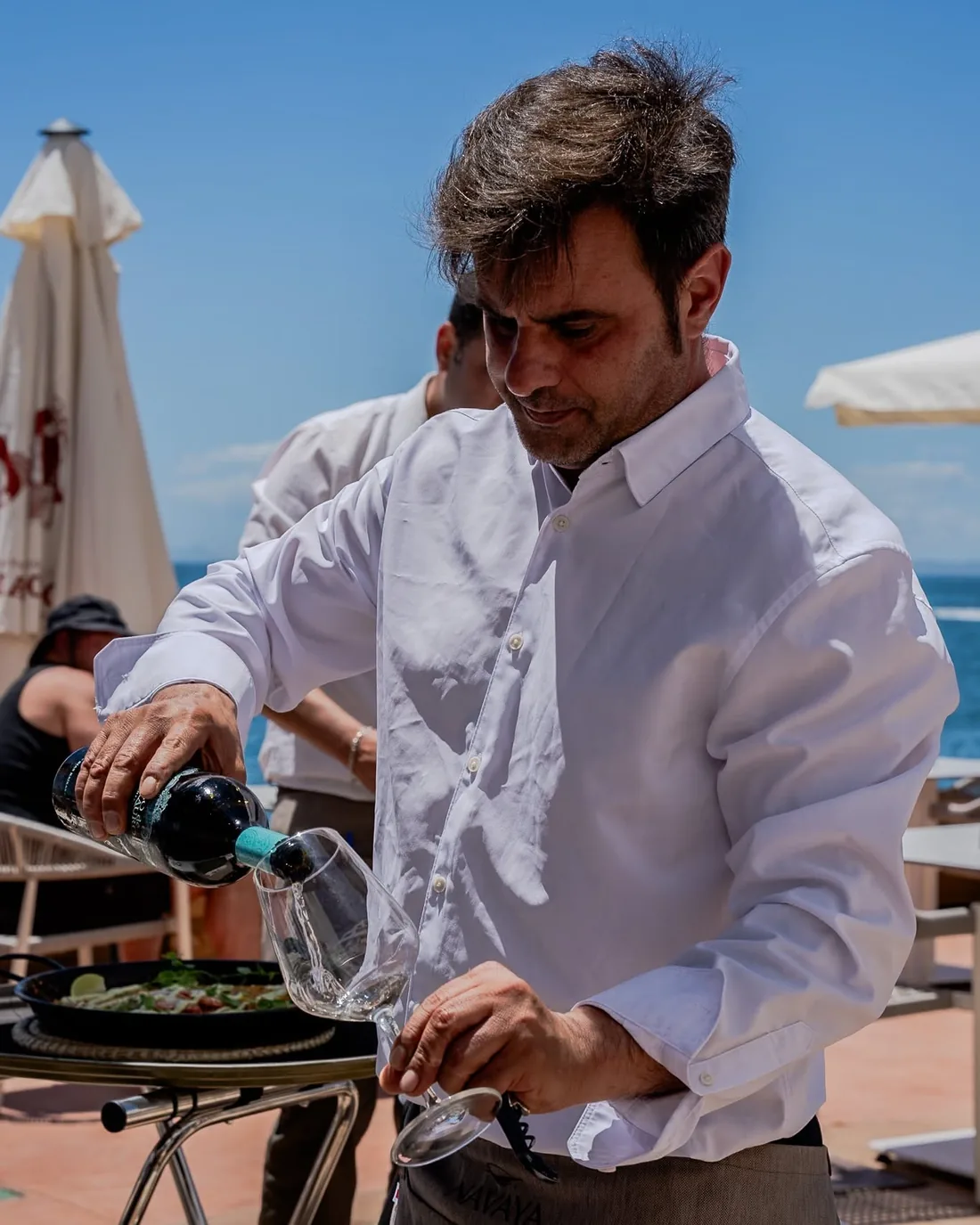 Waiter pouring wine on the terrace with the sea behind